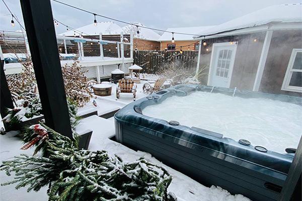 An outdoor Jacuzzi tub filled with clear water and surrounded by beige tiles. The tub features several jets and has a headrest at one end. Soft lighting illuminates the space, creating a serene and relaxing atmosphere